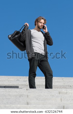 guy on stairs with phone, thoughtful young man sitting on a flight of steps staring into the distance with a serious expression against a blue sky background, guy with sport bag, copy space