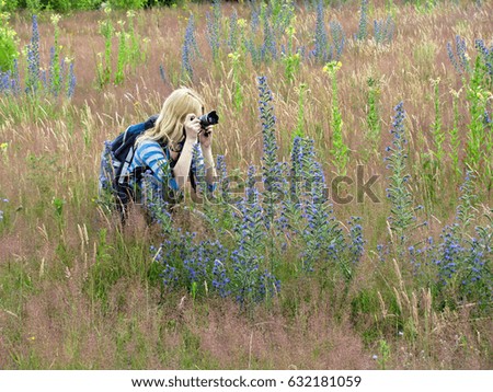 The girl is sitting among the grass and taking pictures