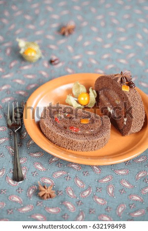 Two pieces of Chocolate Swiss Roll Cake with dried and candied fruit filling, on orange plate, on grey background.