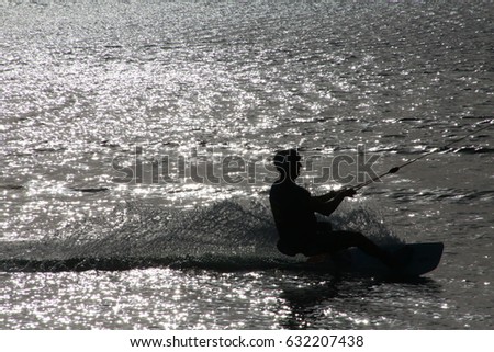Wake Boarder Being Pulled by Cable Down Low Creating Spray Left to Right in Silhouette Late Afternoon against Sunlit Water Sparkles in Ski Rixen Lake, Quiet Waters Park, Deerfield Beach, Florida