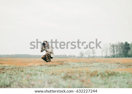 Nature photographer sitting down in grassy area taking pictures.
