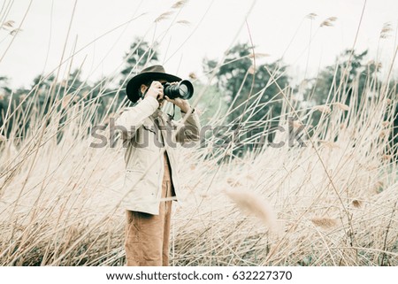 Man with hat standing between reed photographing nature.