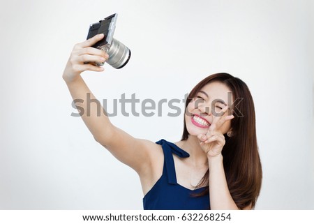 Happy asian woman smiling while taking selfie with mirrorless camera in front of white background
