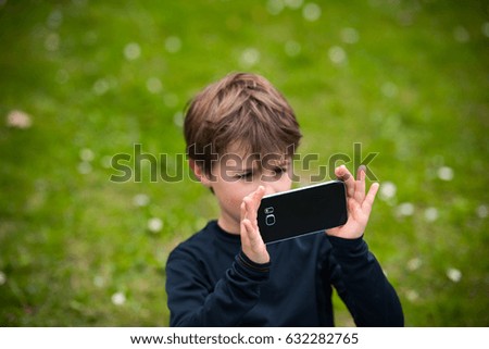 Young boy taking a photo with his phone at the park