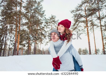 Love - Happy couple having fun smiling laughing together on romantic holidays. Young man giving piggyback ride to his girlfriend outdoor in winter park.