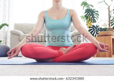 Cropped shot of appealing young woman being in lotus posture while sitting on yoga mat