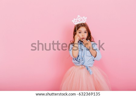 Surprised pretty young girl in tulle skirt with crown on head expressing isolated on pink background. Amazing cute little princess at carnival. Place for text Royalty-Free Stock Photo #632369135