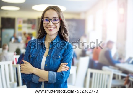 Lets work together. Portrait of young smiling brunette business woman in glasses at modern startup office interior with team in meeting on background.