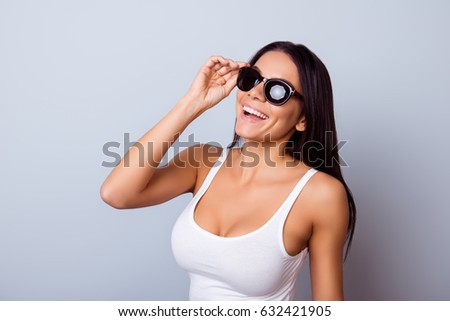 Young cute latin american lady with beaming smile in stylish spectacles is standing on the light blue background. She is full of dreams and fantasies