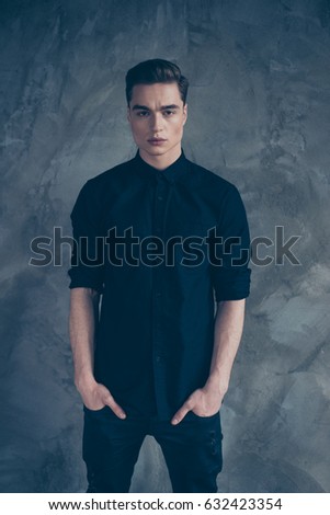 Portrait of young very handsome guy in black outfit looking straight in the camera, behind is grey background Royalty-Free Stock Photo #632423354