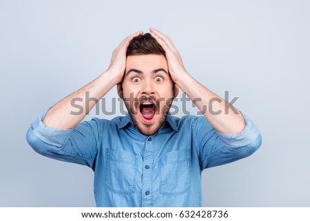 Omg! No way! Very shocked young man is holding his head with bith hands. He is wearing stylish jeans shirt Royalty-Free Stock Photo #632428736