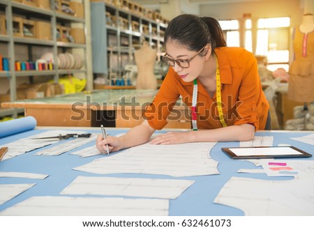 authentic photo of fashion woman designer drawing design sketch working in pattern office studio writing note with mobile computer showing profession and job occupation concept.