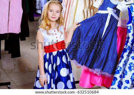 Pretty little girl child choosing a new dress in the shop of children's clothes. Seasonal sale and shopping. Kid's fashion.