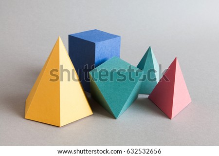 Colorful platonic solids, abstract geometric figures on gray background. Pyramid prism rectangular cube yellow blue pink green colored shapes. Shallow depth of field, copy space.
