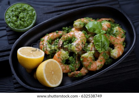 Close-up of a frying pan with tiger shrimps served with parsley sauce and lemon, selective focus