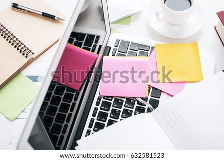 Top view of messy office table with laptop keyboard, coffee cup, colorful supplies and other items
