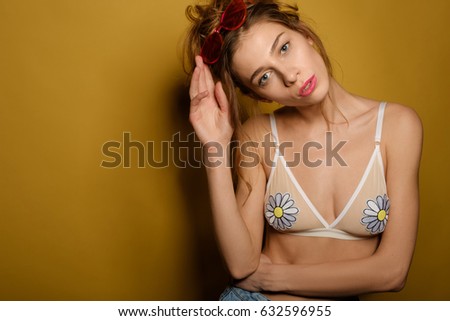 The girl with collected hair and the top of the bathing suit stands on a yellow background with bowed head and lifting the rose-colored glasses on the forehead. Horizontal photo