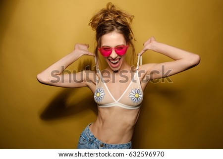 Emotional photo of a girl in a bathing suit and pink glasses pulls the straps up top on a yellow background. Horizontal photo
