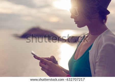 Stylish young woman with mobile phone in hands on the seashore. Communication and roaming during the holidays and travel around the world
