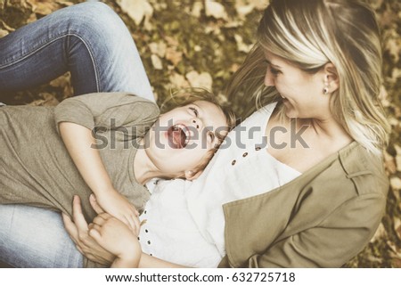 Mother with her daughter playing in the park. Little girl lying on mother lap.