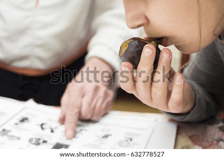 A little girl eating a fruit and listening a teacher pointing a finger in a book, Selective focus cropped shot