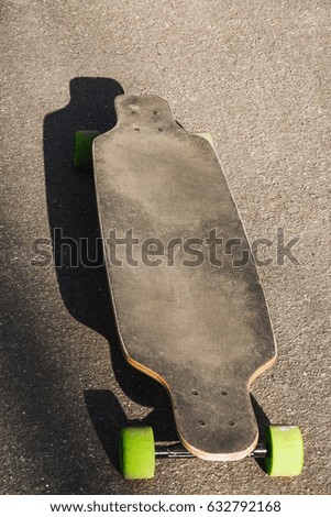 Old used longboard on the asphalt. Old style. Black skateboard on an empty asphalt road.