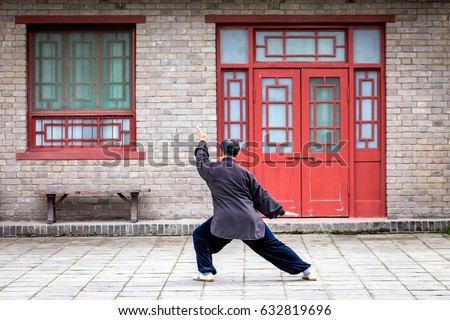 
A Chinese man dressed in black, realizes figures of Kung fu, alone in front of a Chinese house