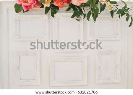Garland of pink and orange flowers hangs over the empty white frames