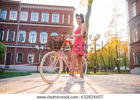 Portrait of a happy beautiful young girl with vintage bicycle and flowers on city background in the sunlight outdoor. Cruiser with basket full of flowers. Active Leisure Concept.