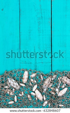 Blank antique rustic wood sign with fish net and seashells border; background with teal blue copy space 