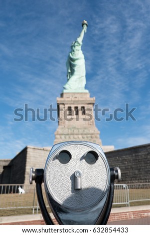 Old tower viewer binoculars in foreground, Statue of Liberty in the background on a sunny day with blue skies on Liberty Island, Manhattan, New York City. Statue of Liberty in profile on her pedestal.