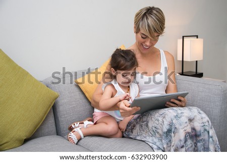 Cheerful mother showing game on tablet to daughter
