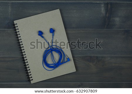 note book with earphones on wooden background 