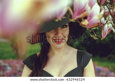 Beautiful girl with black hair in a black dress on a background of a magnolia flower. Blurring background. Shooting outdoors. The concept of fashion and beauty. Beautiful girl and magnolia flowers. 