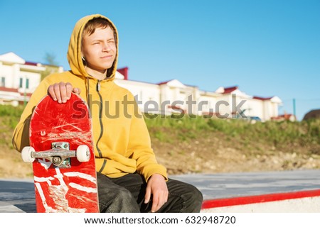 Close-up of a teenager dressed in a jeans hoodie sitting in a skate park and holding a skateboard