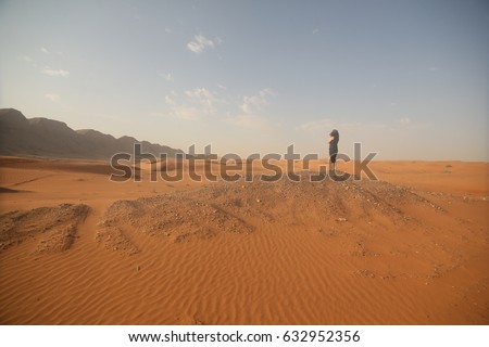 a lady photographer in desert area, sand, rock background, wear black shirt. - United Arab Emirates