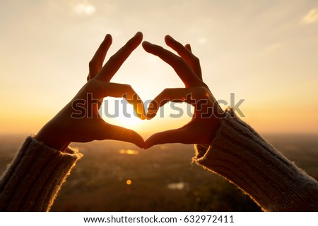 Female hands in the form of heart against the sky pass sun beams. Hands in shape of love heart.