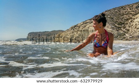 The girl enjoys the warm sea, in front of the background of high rocks.