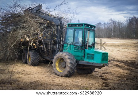Big green tractor with cut trees and timber, placed on the field in village, to make a new road