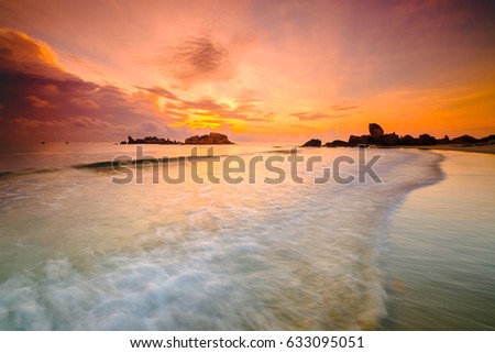 Soft wave of the turquoise sea on the sandy beach. Natural sunrise and rock island as background at Pantai Penunjuk ,Malaysia. Image contain grain and motion blur effect