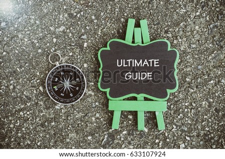word ultimate guide written on wooden easel with compass. with flare and lighting effect concept image
