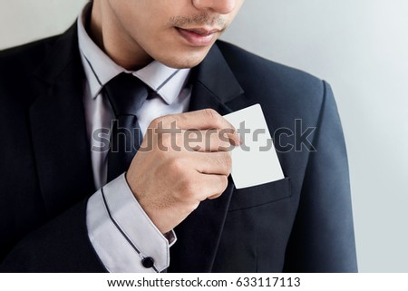 Upper part of Businessman in black suit pulling blank business card from his pocket, Selective focus on face and hand, card as clipping path