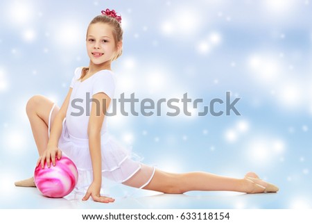 Beautiful little girl gymnast dressed in sports suits for competition, performs exercises with the ball.Blue Christmas festive background with white snowflakes.