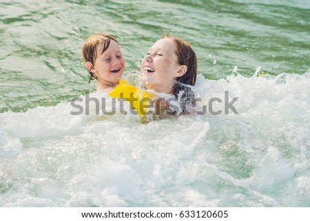Young mother swimming and playing with male child boy in sea or ocean water sunny day outdoor on natural background, horizontal picture.