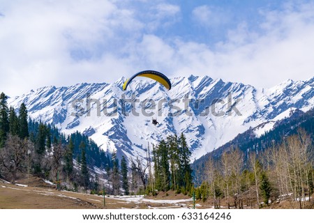 Paragliding at Solang Valley with Snow cladded mountains of Dhauladhar in background en-route to Rohtang Pass, Manali, Himachal Pradesh, India. Royalty-Free Stock Photo #633164246