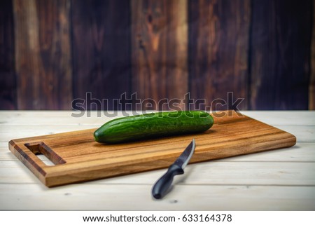Green cucumber on a cutting board and a kitchen knife