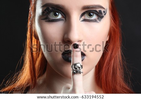 Red-haired girl with black make-up shows finger on black background