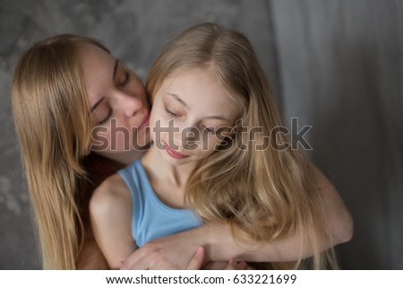 Mom and daughter teenager blonde with long hair hug and adoption, gray lifestyle in a real interior. Motherhood concept closeup