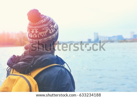A woman traveler looks out into distance on a city through a lake. Outside the city, the tourist admires the beauty of the landscape. Concept travel, walking with backpack, a healthy lifestyle, dreams