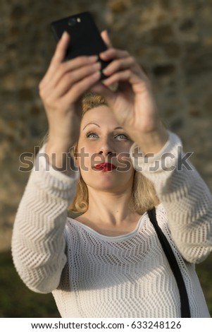 Blonde girl taking selfie with her smartphone, looking up. Shot from above. 